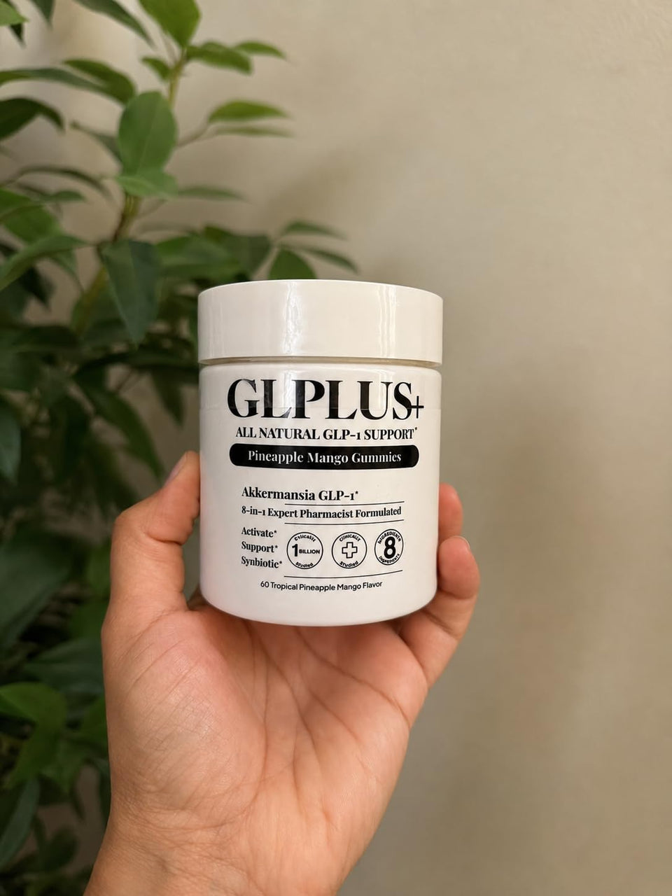 Customer holding a GLPLUS+ pineapple mango gummies jar beside a green plant.