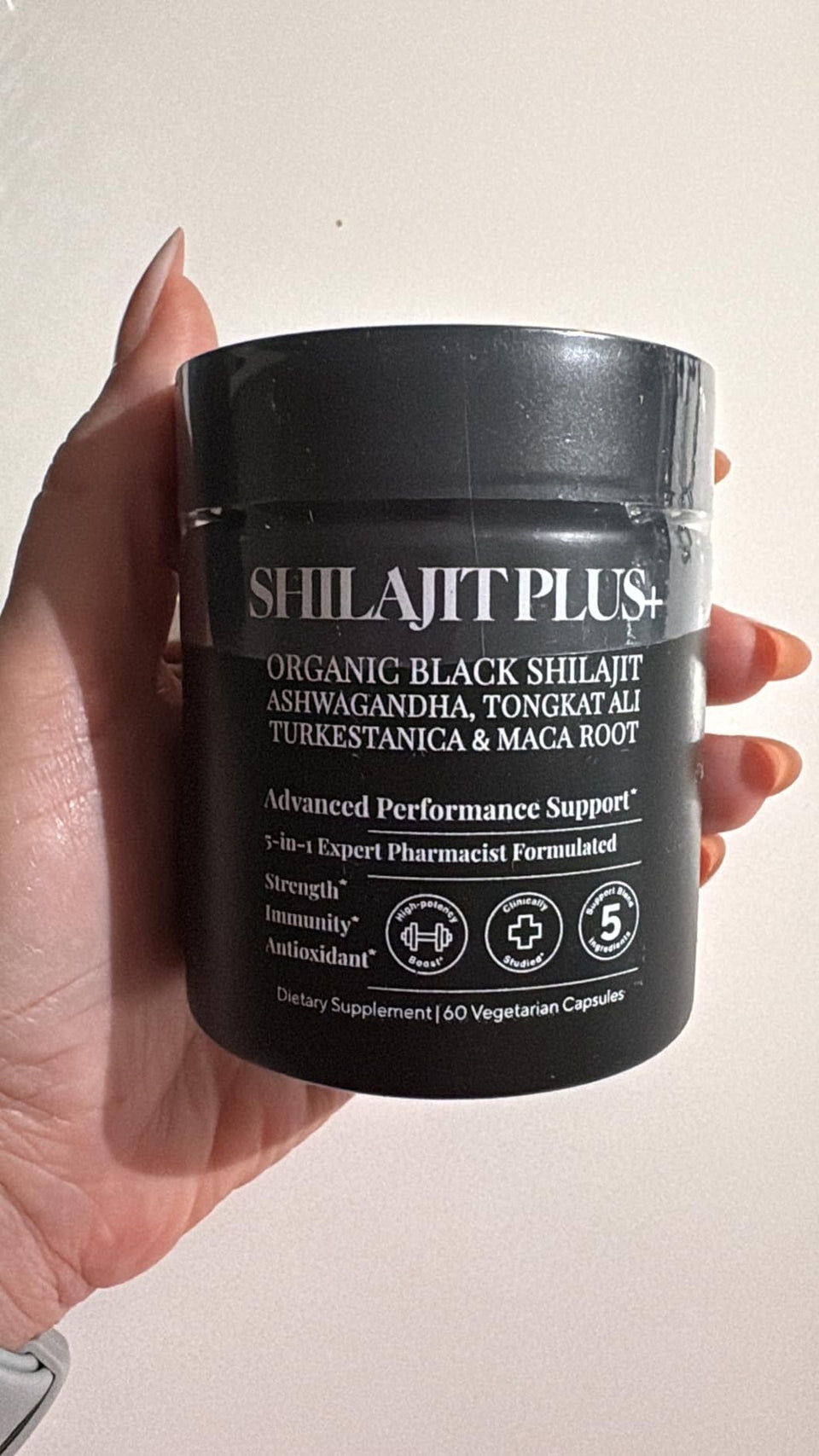 Customer holding a black SHILAJITPLUS+ jar against a light wall.